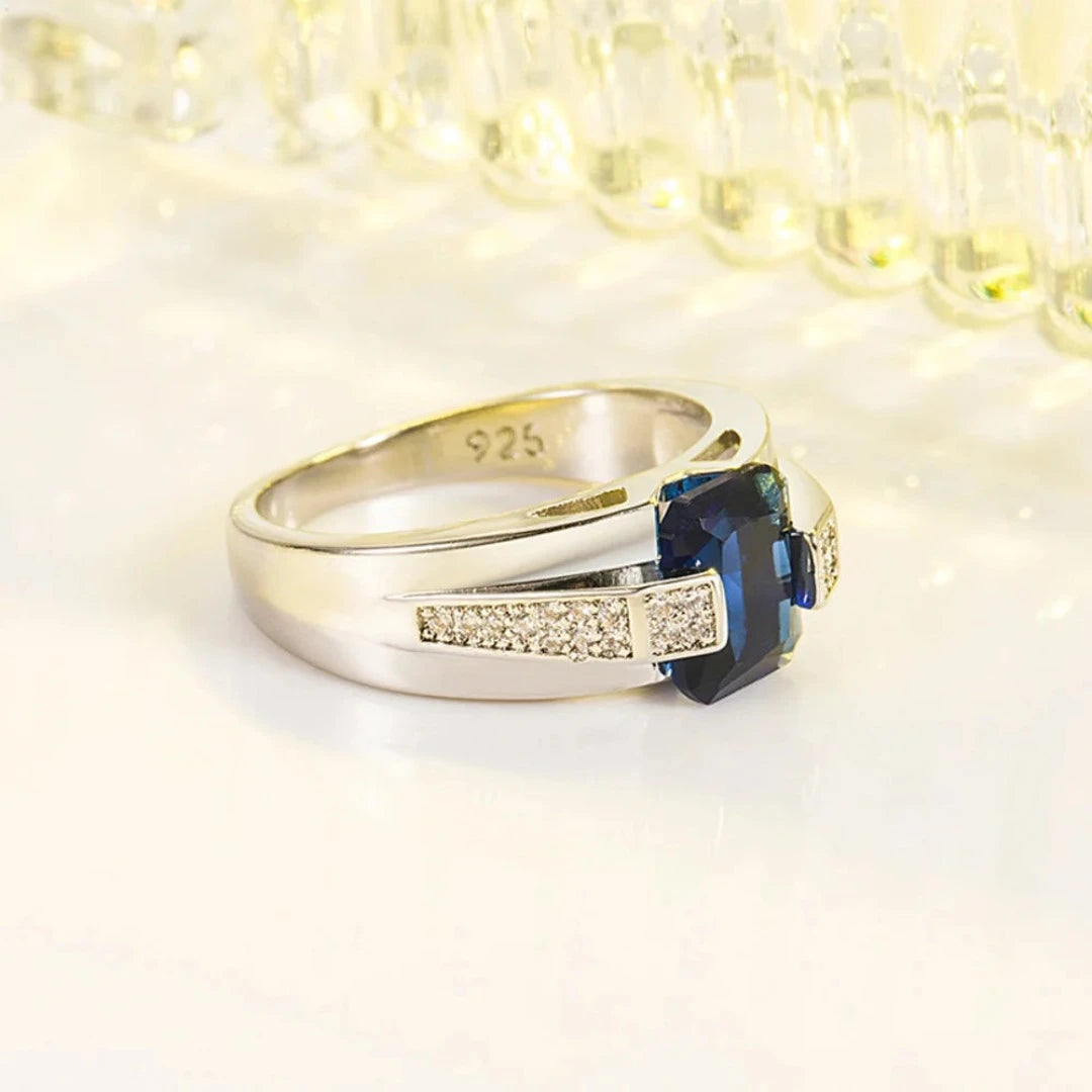 Fabricado com prata 925 de alta qualidade, este anel apresenta um acabamento polido que realça a beleza natural do metal precioso. O destaque indiscutível é a pedra azul central, que captura a luz de maneira fascinante, adicionando um toque de glamour e mistério à peça.